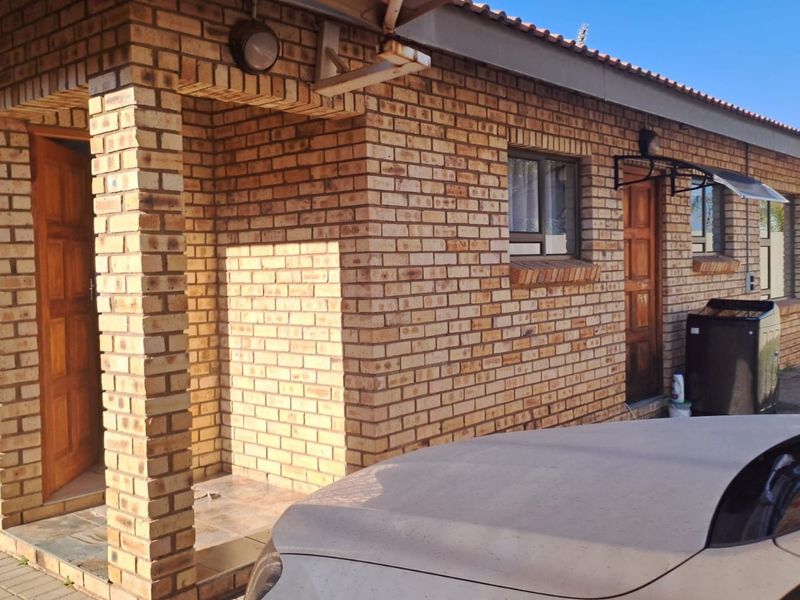 Exterior view of a face brick house featuring a covered entrance, wooden doors, and paved walkway.
