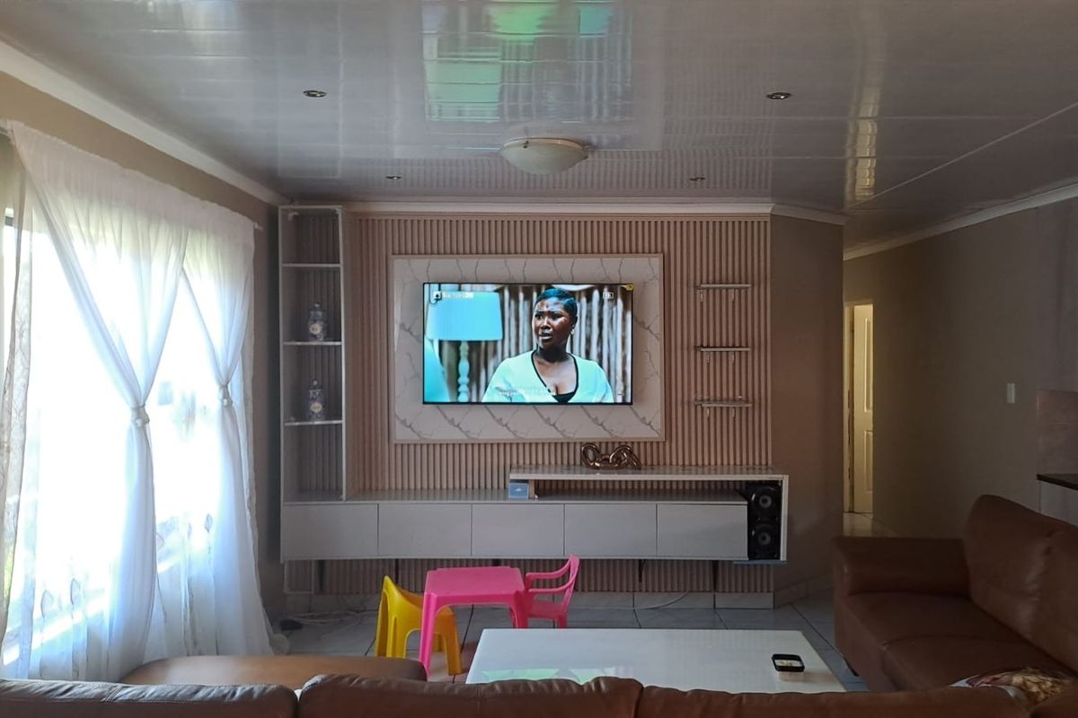 A well-maintained living room featuring a modern built-in media unit with slatted wall paneling, recessed lighting, and tiled flooring.