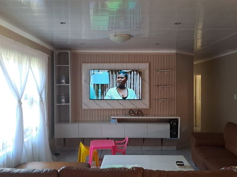 A well-maintained living room featuring a modern built-in media unit with slatted wall paneling, recessed lighting, and tiled flooring.