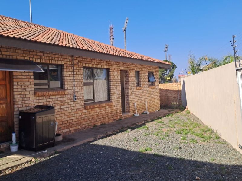 Rear view of a face brick house featuring a tiled roof, paved walkway, and secure boundary wall with electric fencing.