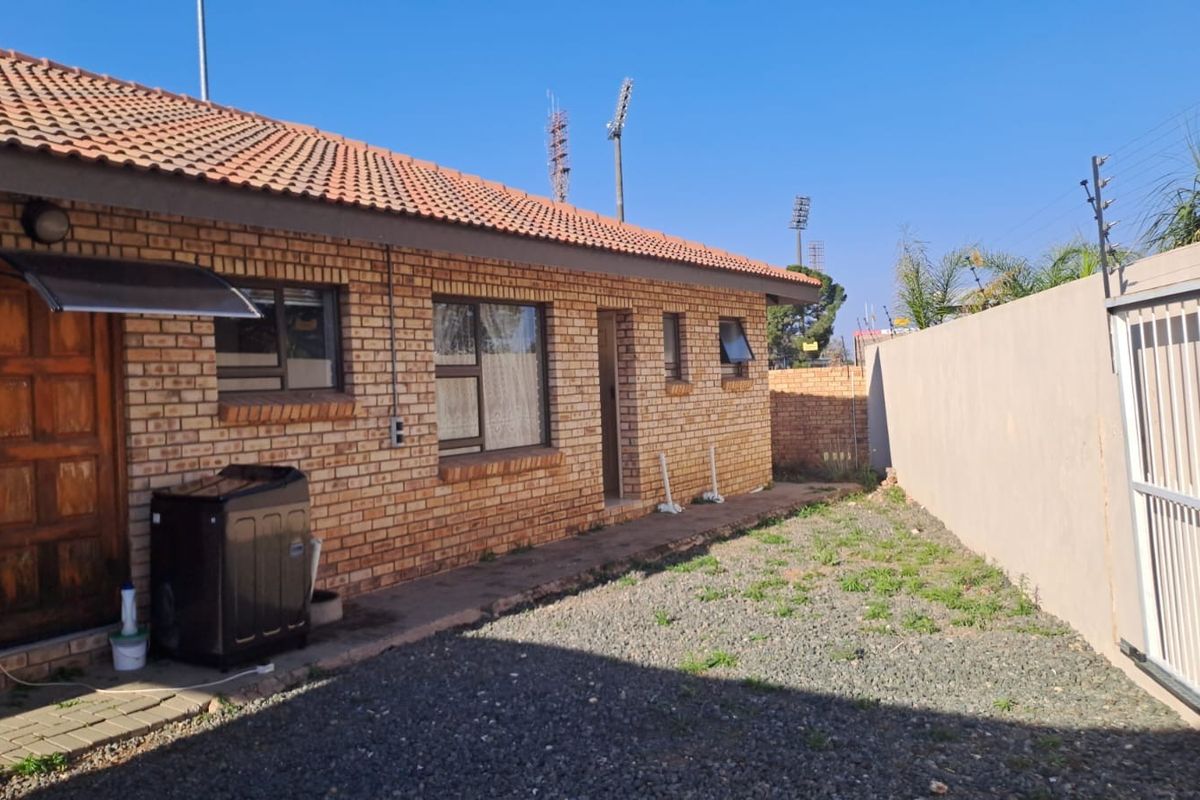 Rear view of a face brick house featuring a tiled roof, paved walkway, and secure boundary wall with electric fencing.
