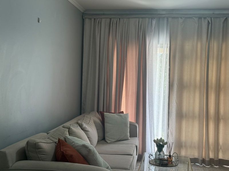 A living room area featuring neutral wall tones and floor-to-ceiling curtains covering a sliding door, providing access to the exterior.