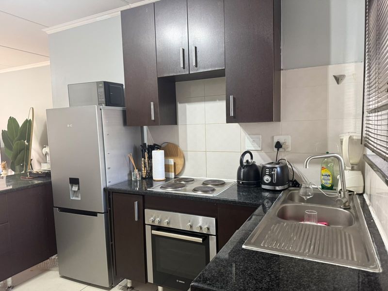 A functional kitchen featuring dark wood cabinetry, granite countertops, a stainless steel sink, and built-in electric oven and hob.
