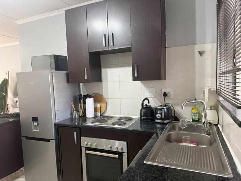 A compact kitchen featuring dark wood cabinetry, granite countertops, a stainless steel sink, and built-in oven with electric hob.