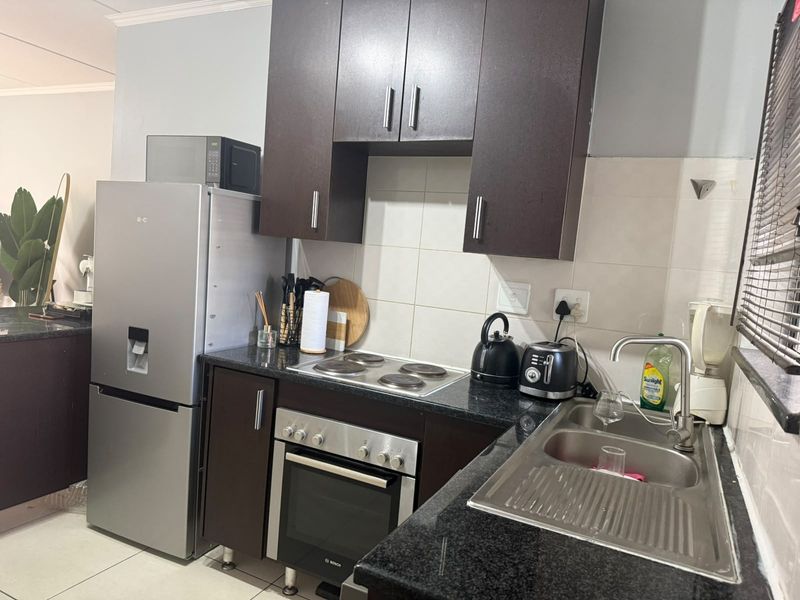 A compact kitchen featuring dark wood cabinetry, granite countertops, a stainless steel sink, and a built-in oven with an electric hob.