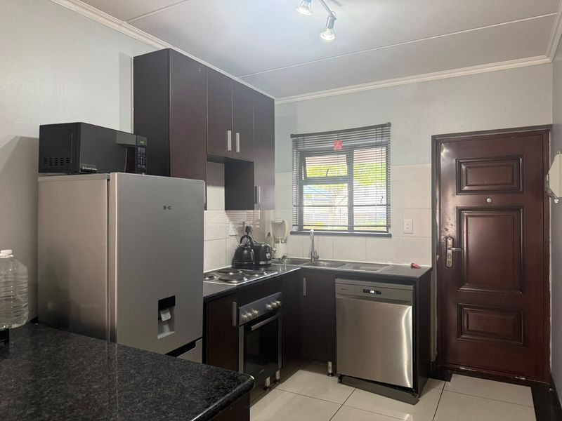 Compact kitchen featuring dark wood cabinetry, granite countertops, built-in oven, electric hob, and tiled flooring with direct access to an exterior door.