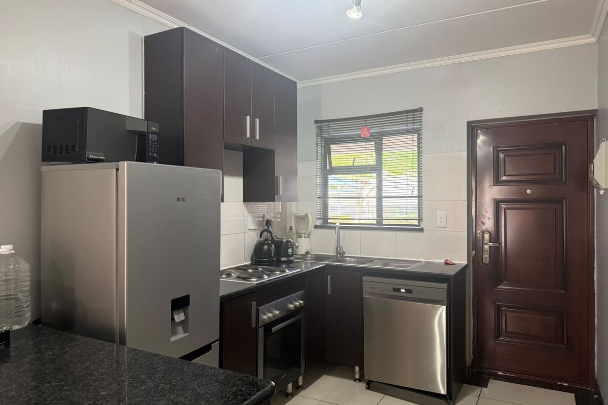Compact kitchen featuring dark wood cabinetry, granite countertops, built-in oven, electric hob, and tiled flooring with direct access to an exterior door.