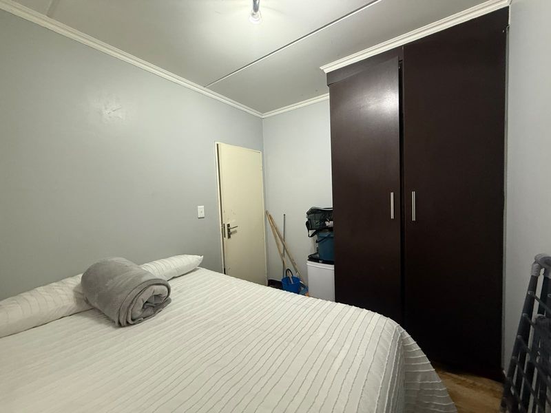 A functional bedroom featuring a dark wood built-in wardrobe, laminate flooring, and crown molding, offering a neutral base for potential interior updates.