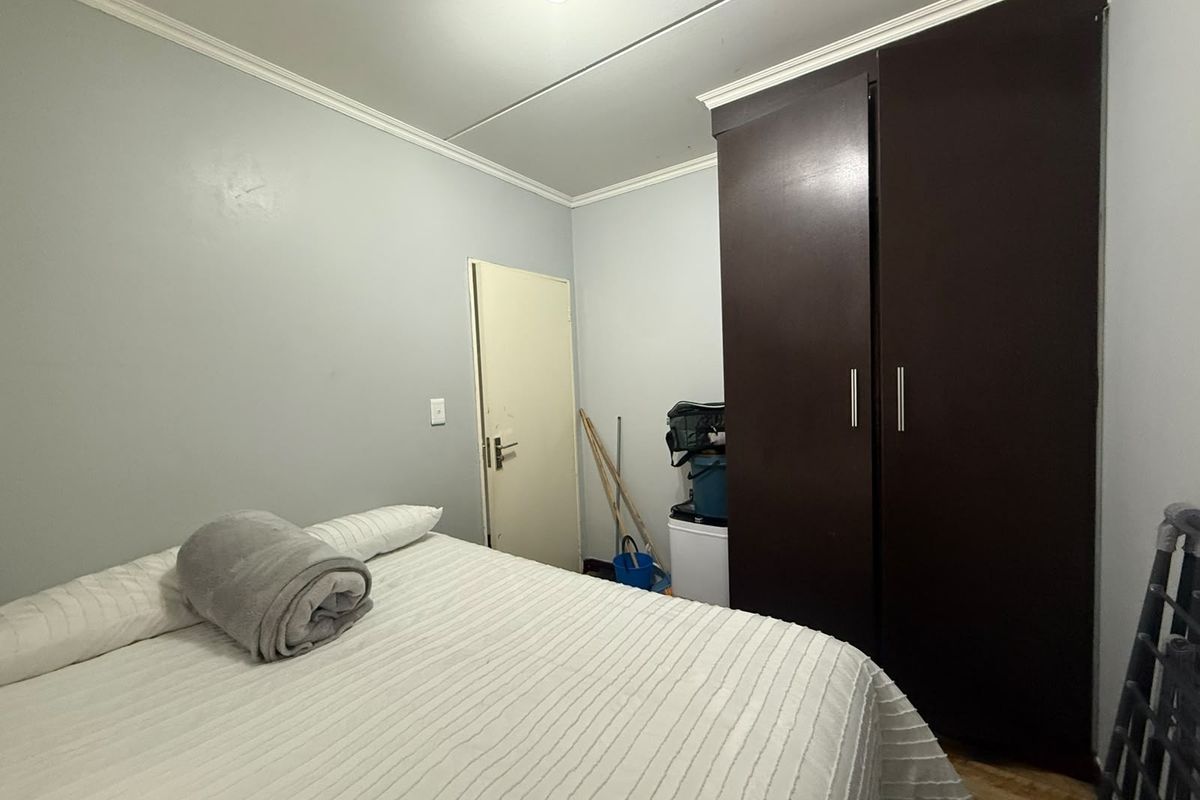 A functional bedroom featuring a dark wood built-in wardrobe, laminate flooring, and crown molding, offering a neutral base for potential interior updates.