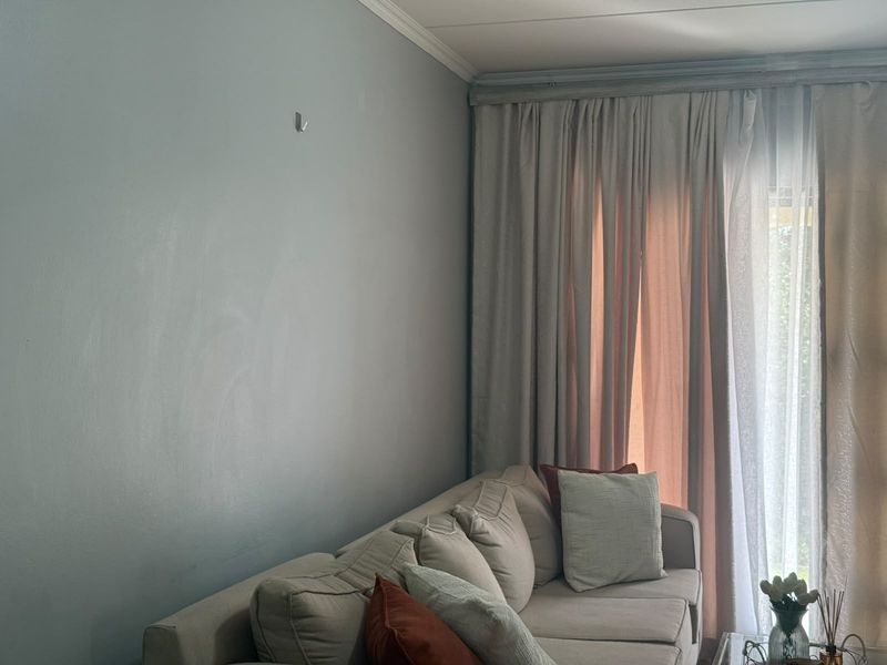 A living room area featuring neutral wall paint, crown molding, and floor-to-ceiling curtains covering a large window or sliding door.