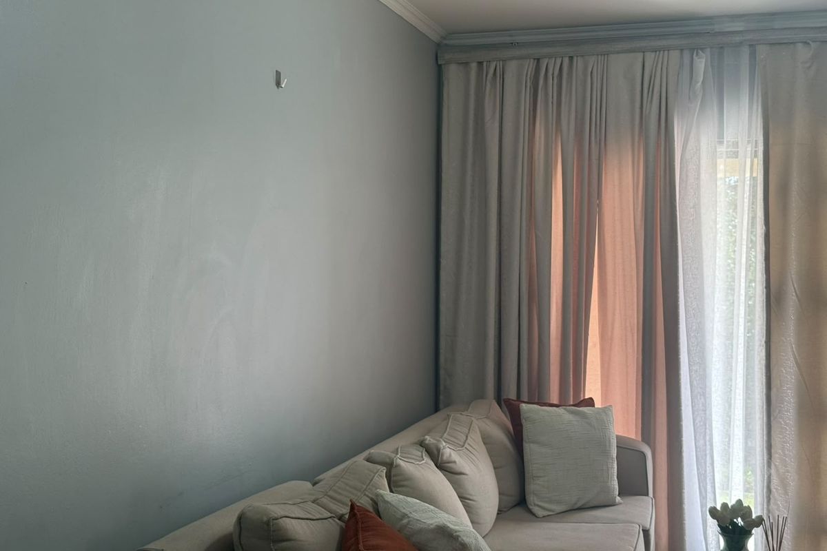 A living room area featuring neutral wall paint, crown molding, and floor-to-ceiling curtains covering a large window or sliding door.