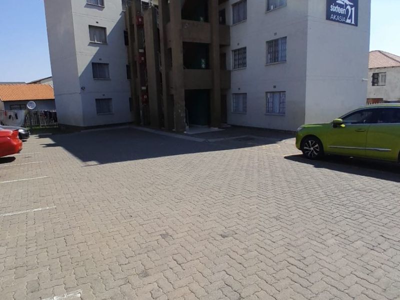 Exterior view of the Sixteen Akasia apartment complex featuring a paved parking area and multi-story residential building facade.
