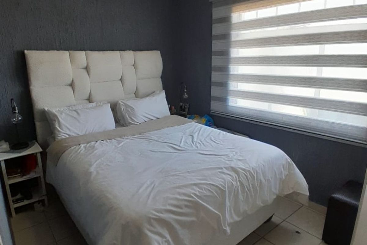 A compact bedroom featuring tiled flooring, dark textured walls, and a window fitted with modern roller blinds.