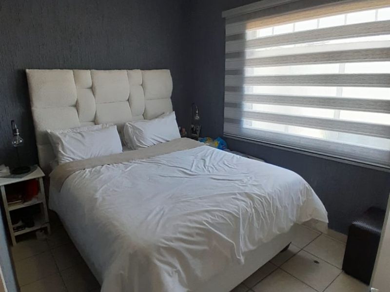 A compact bedroom featuring tiled flooring, dark textured walls, and a window fitted with modern roller blinds.