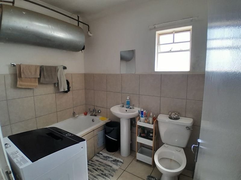A functional bathroom featuring a pedestal basin, bathtub, and toilet, with tiled finishes and an exposed geyser unit.