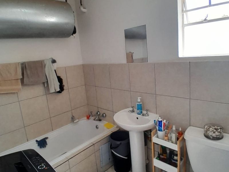 A functional bathroom featuring a pedestal basin, bathtub, and toilet with neutral wall and floor tiling and an exposed geyser unit.