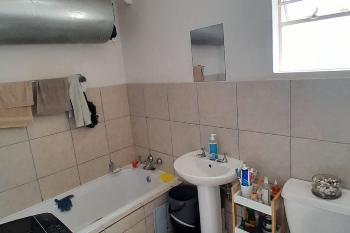 A functional bathroom featuring a pedestal basin, bathtub, and toilet with neutral wall and floor tiling and an exposed geyser unit.
