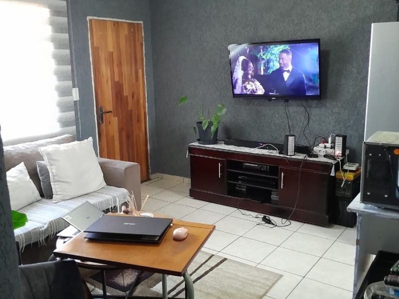 A living room featuring tiled flooring, a textured dark feature wall, and roller blinds, providing a functional and comfortable living space.