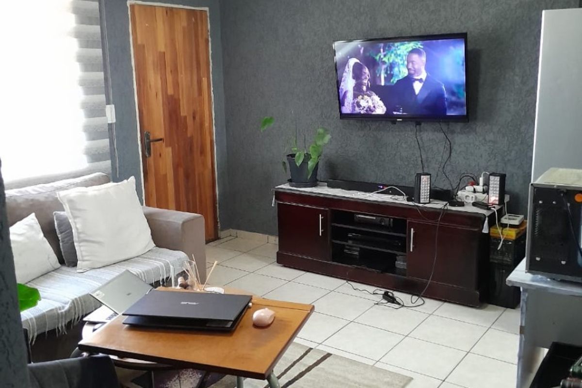 A living room featuring tiled flooring, a textured dark feature wall, and roller blinds, providing a functional and comfortable living space.