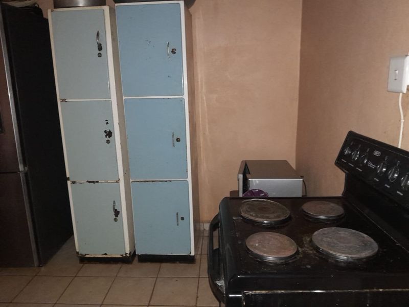 A basic kitchen area featuring a freestanding electric stove, tiled flooring, and dated metal storage lockers.