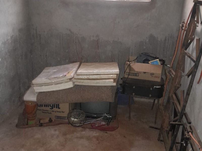 An unfinished utility space featuring raw concrete walls and flooring with security bars on the window, requiring significant renovation and finishing.