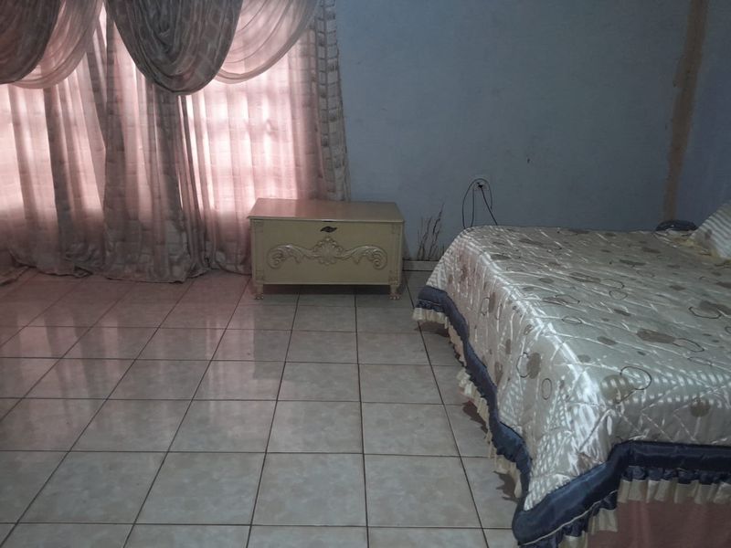 A bedroom featuring tiled flooring and window treatments, showing signs of wear on the walls requiring maintenance and cosmetic updates.