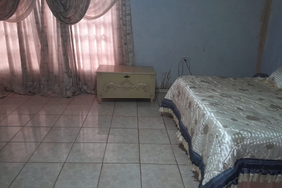 A bedroom featuring tiled flooring and window treatments, showing signs of wear on the walls requiring maintenance and cosmetic updates.