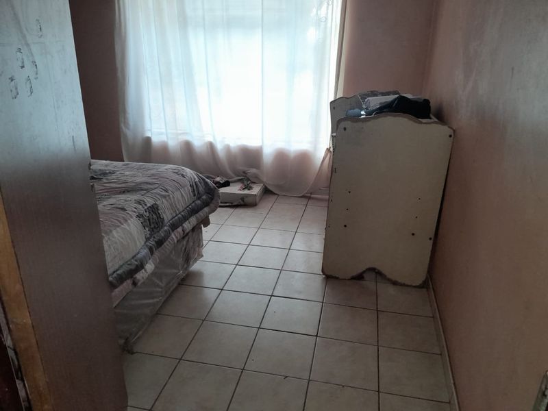 A bedroom featuring tiled flooring and a window with sheer curtains, requiring cosmetic updates to the wall finishes.