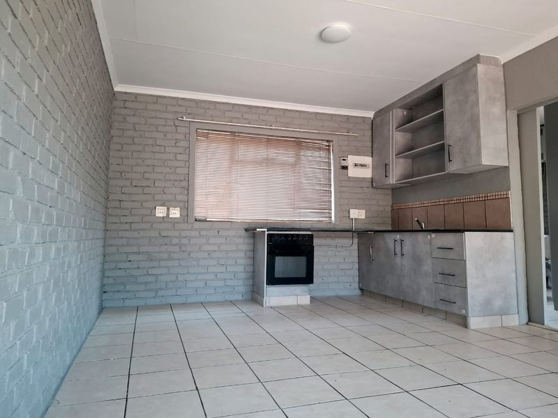 A functional kitchen featuring grey cabinetry, an integrated oven and hob, tiled flooring, and an exposed brick feature wall.