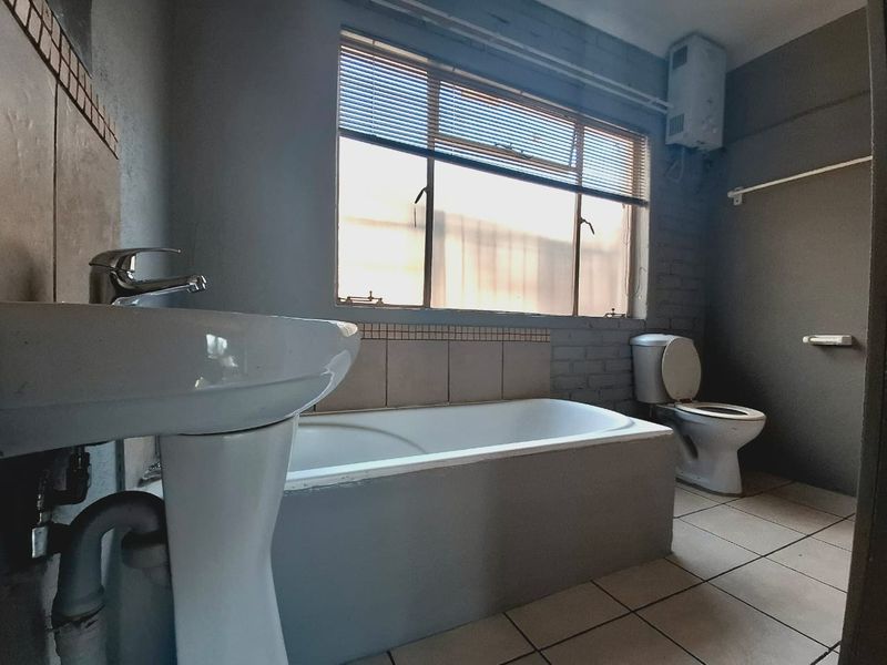 A functional bathroom featuring a pedestal basin, bathtub, and toilet, with tiled flooring and a wall-mounted gas geyser.