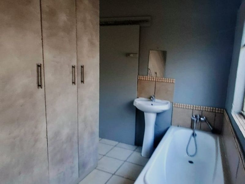 A functional bathroom featuring a pedestal basin, built-in bathtub, and ample built-in storage cupboards with tiled flooring throughout.