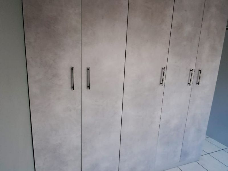 A bedroom featuring modern grey built-in cupboards and clean tiled flooring, offering ample storage space.