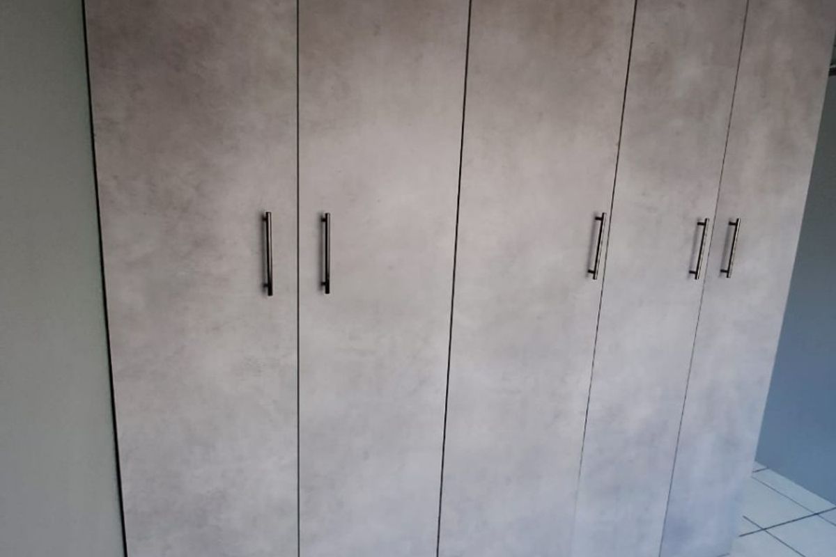 A bedroom featuring modern grey built-in cupboards and clean tiled flooring, offering ample storage space.