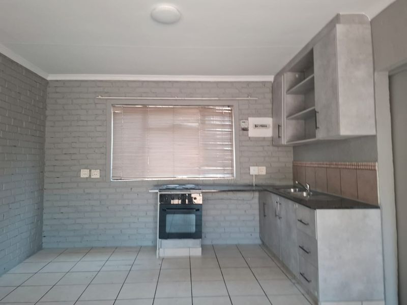 A functional kitchen featuring grey cabinetry, a built-in electric stove and oven, double sink, and tiled flooring against an exposed brick wall.