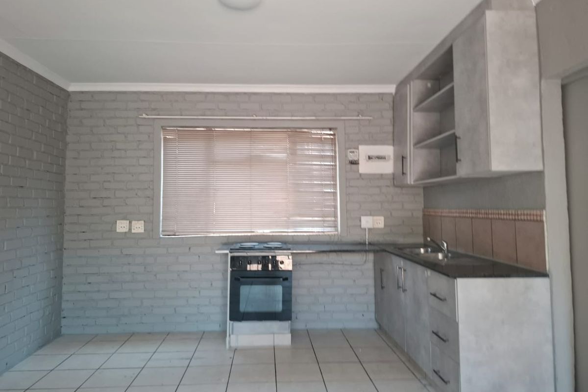 A functional kitchen featuring grey cabinetry, a built-in electric stove and oven, double sink, and tiled flooring against an exposed brick wall.