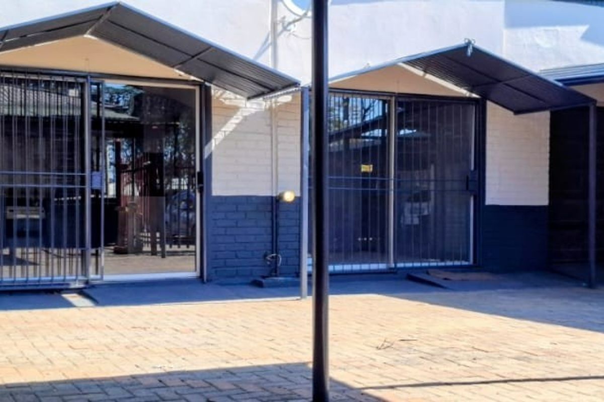 A paved rear courtyard area featuring metal awnings, security gates, and sliding glass door access to the apartment.