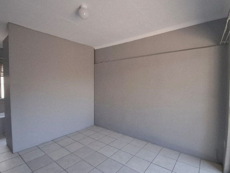 An empty bedroom featuring neutral grey walls, tiled flooring, and a ceiling light fixture, ready for personalization.