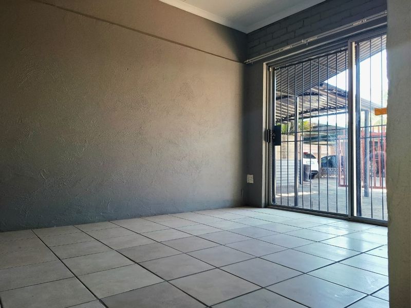 An empty living room featuring tiled flooring and a sliding glass door with a security gate, providing direct access to the exterior.
