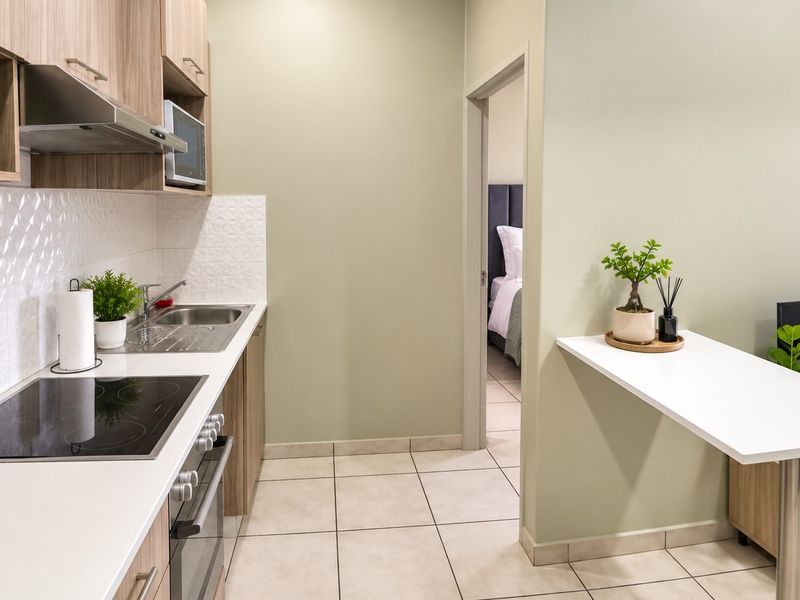 Modern open-plan kitchen featuring light wood cabinetry, electric hob, built-in oven, and a convenient breakfast bar, seamlessly connecting to the adjacent living and bedroom areas.