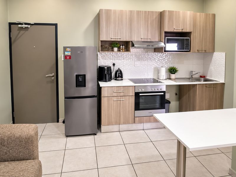 Modern open-plan kitchen featuring wood-finish cabinetry, integrated appliances, a textured tile backsplash, and neutral tiled flooring.