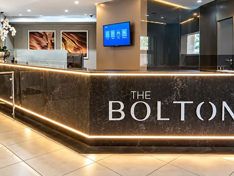 Modern apartment building reception area featuring a sleek marble-look desk with integrated LED lighting and professional security turnstile access.
