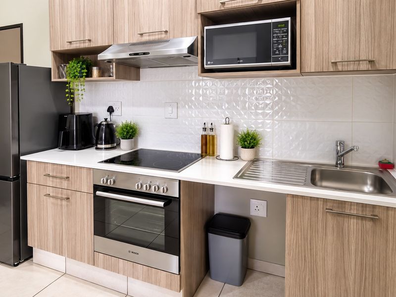 Modern kitchen featuring light wood-grain cabinetry, stone countertops, a tiled backsplash, and integrated stainless steel appliances including an oven, hob, and extractor fan.