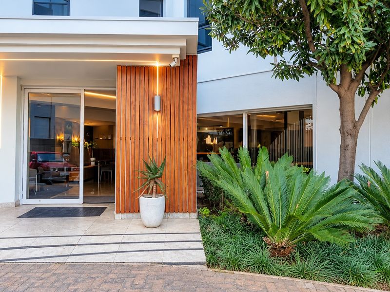 Modern apartment building entrance featuring timber slat cladding, glass sliding doors, and well-maintained landscaped garden area.