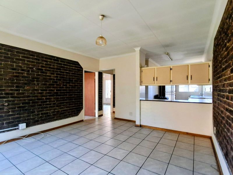 Open plan living and kitchen area featuring exposed brick walls, tiled flooring, and dated cabinetry, offering a blank canvas for renovation.