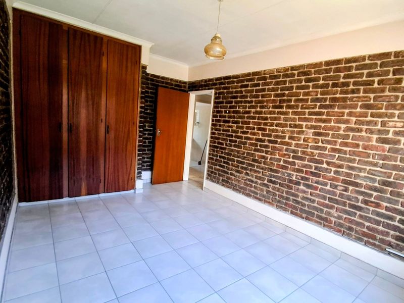 An empty bedroom featuring an exposed brick wall, built-in wooden cupboards, and tiled flooring, offering a blank canvas for personalization.