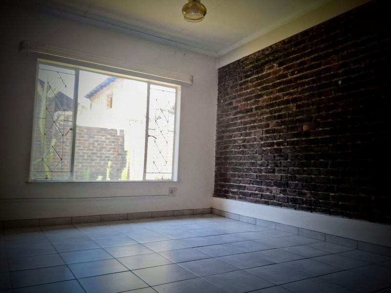 An empty bedroom featuring a rustic exposed brick feature wall, tiled flooring, and a large window with security bars.