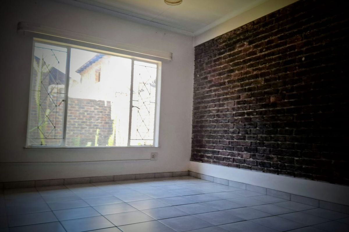 An empty bedroom featuring a rustic exposed brick feature wall, tiled flooring, and a large window with security bars.