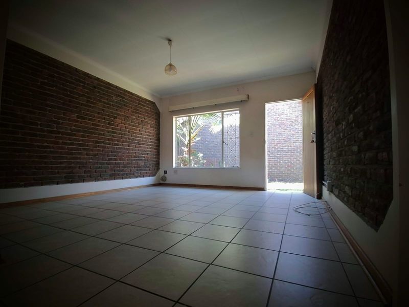 An empty living room featuring exposed brick feature walls, tiled flooring, and direct access to an outdoor area through a doorway.