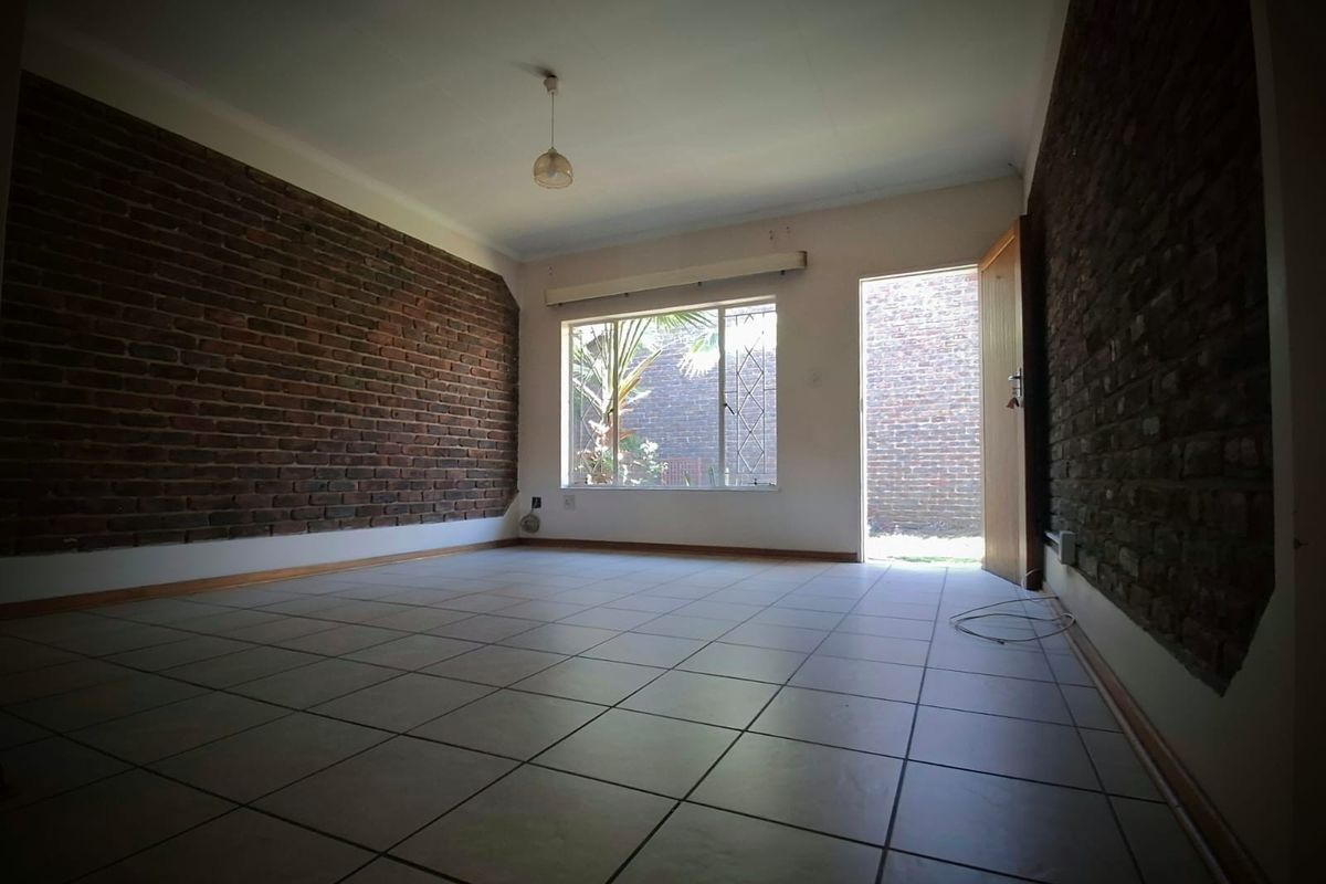 An empty living room featuring exposed brick feature walls, tiled flooring, and direct access to an outdoor area through a doorway.