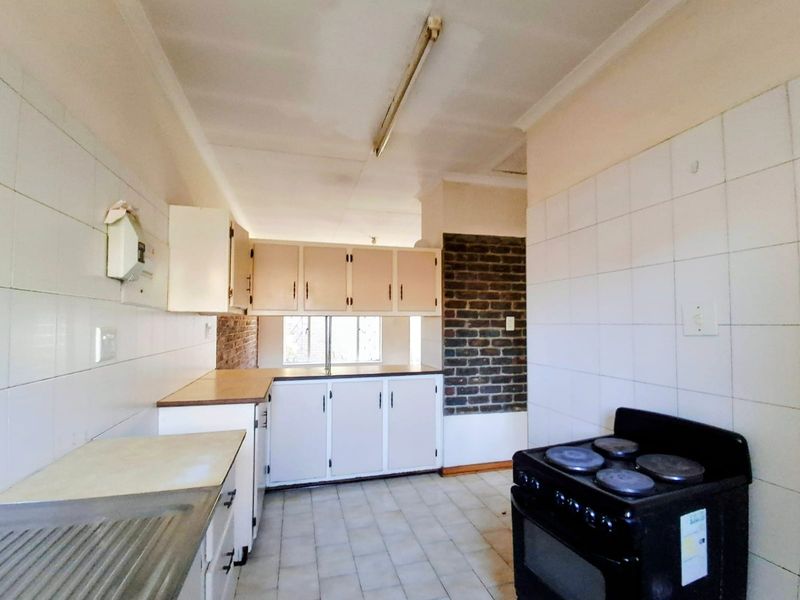 A dated kitchen featuring built-in cabinetry, tiled surfaces, and an exposed brick accent wall, offering a functional layout ready for modernization.